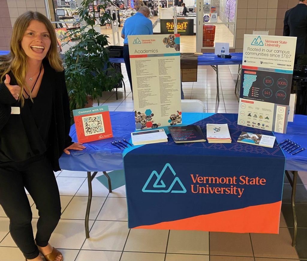 a picture of the same table set up, but with VTSU recruiter sierra verburg standing in front of it with a smile and giving a thumbs up