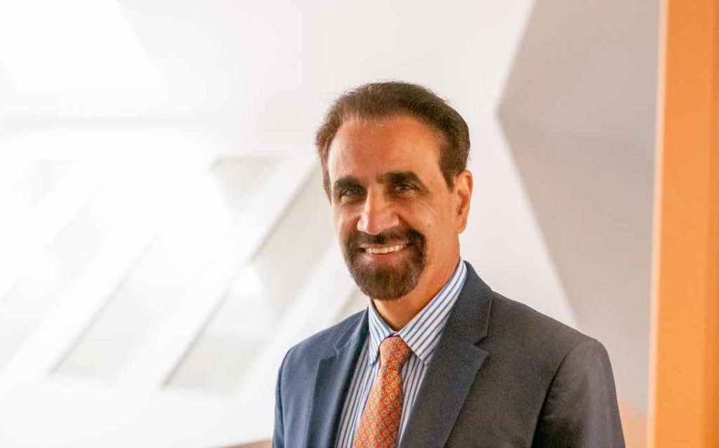 photo of president Grewal in a bright room. he is smiling and wearing a suit.